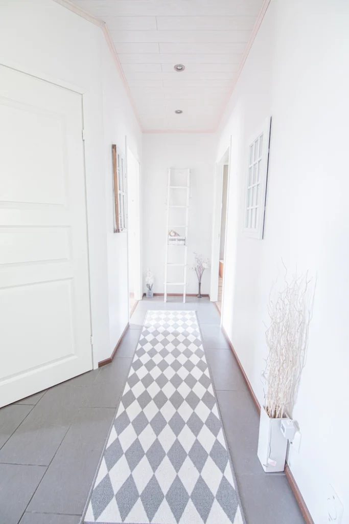 Talon käytävä ja lattialla vaalea matto, jossa on harmaita salmiakkikuvioita. Peräseinällä valkoiset sisistustikapuut.