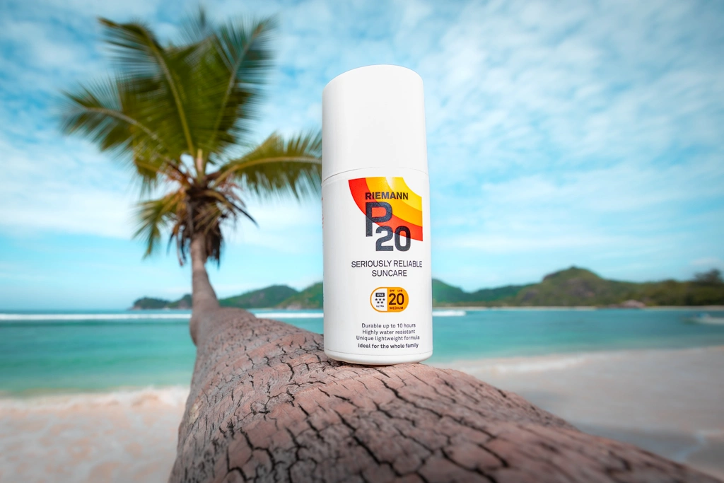 Merenrantamaisema jossa on suoritettu tuotekuvaus ja palmun rungon päällä on aurinkorasvapullo.