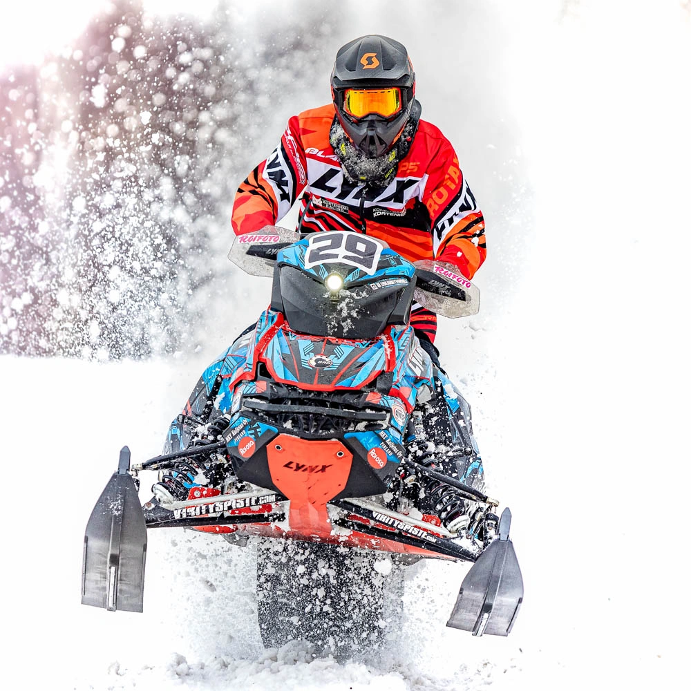 Moottorikelkkailija ajaa kohti kuvaajaa ja lumi pöllyää taustalla.