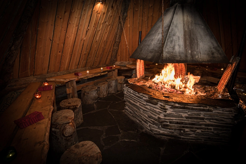 Sisältä kuvattu grillikota, jossa on tulet ja lohia on kypsymässä tulen äärellä.